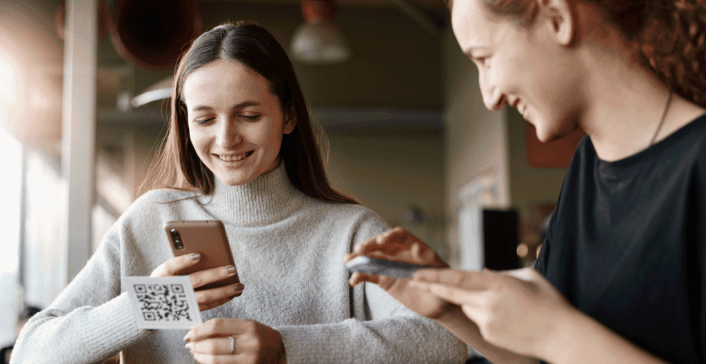 Young woman smiling whilst scanning a QR code with her smartphone for contactless payment in a shop, demonstrating Gen Z mobile payment preferences