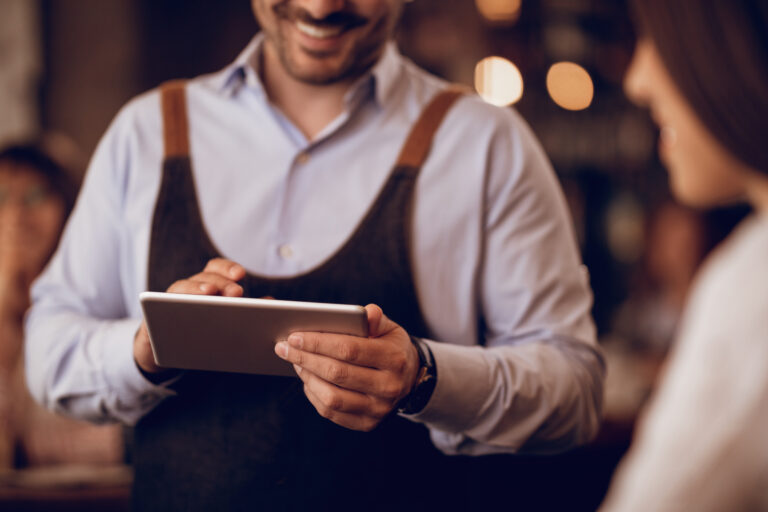 Waiter using tablet for subscription payment processing while serving customer in UK restaurant